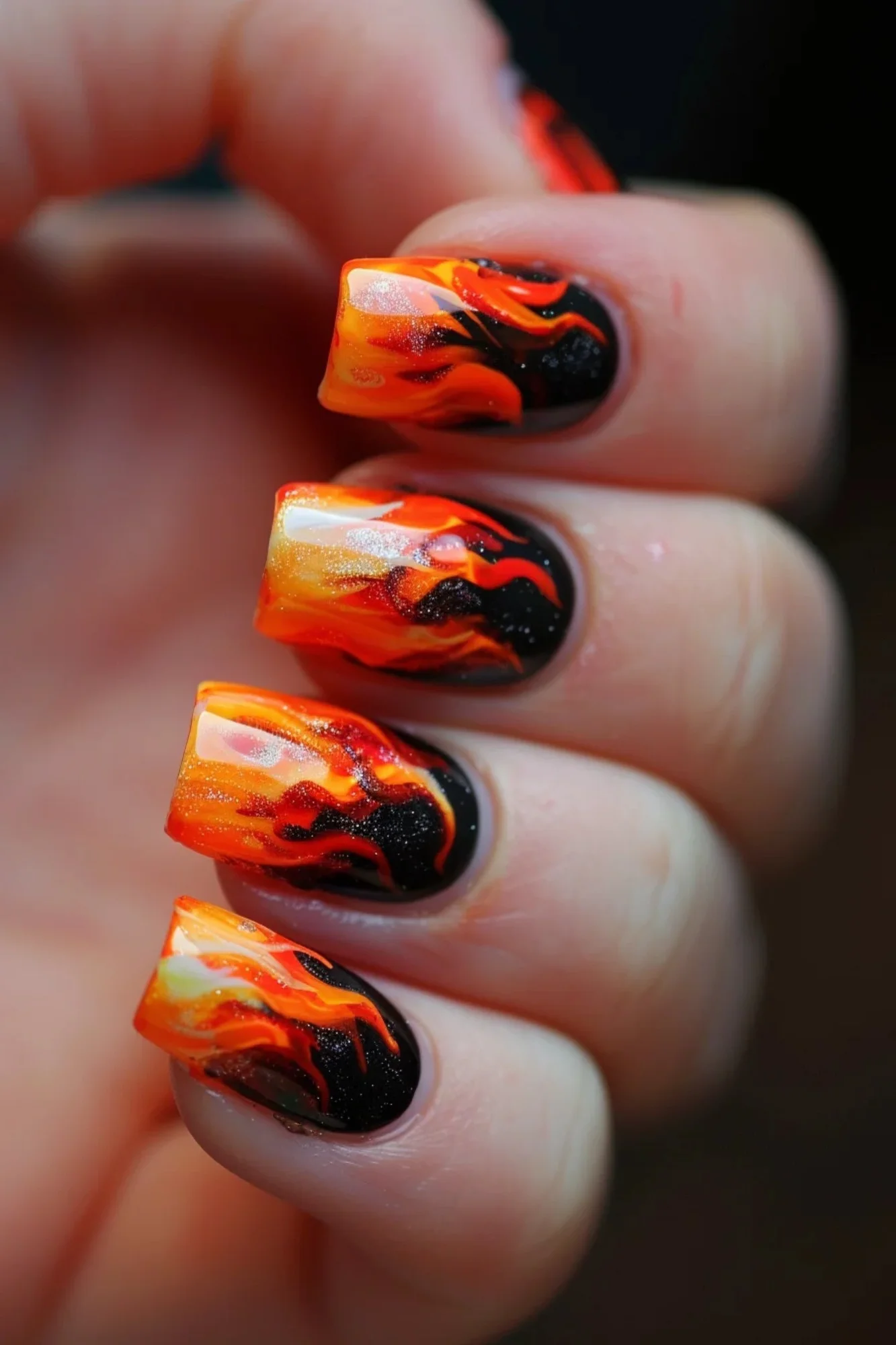 These nails have a deep, dark base color, possibly black, with bright orange flames. The flames are highlighted with yellow and white accents, giving them a glowing effect. T