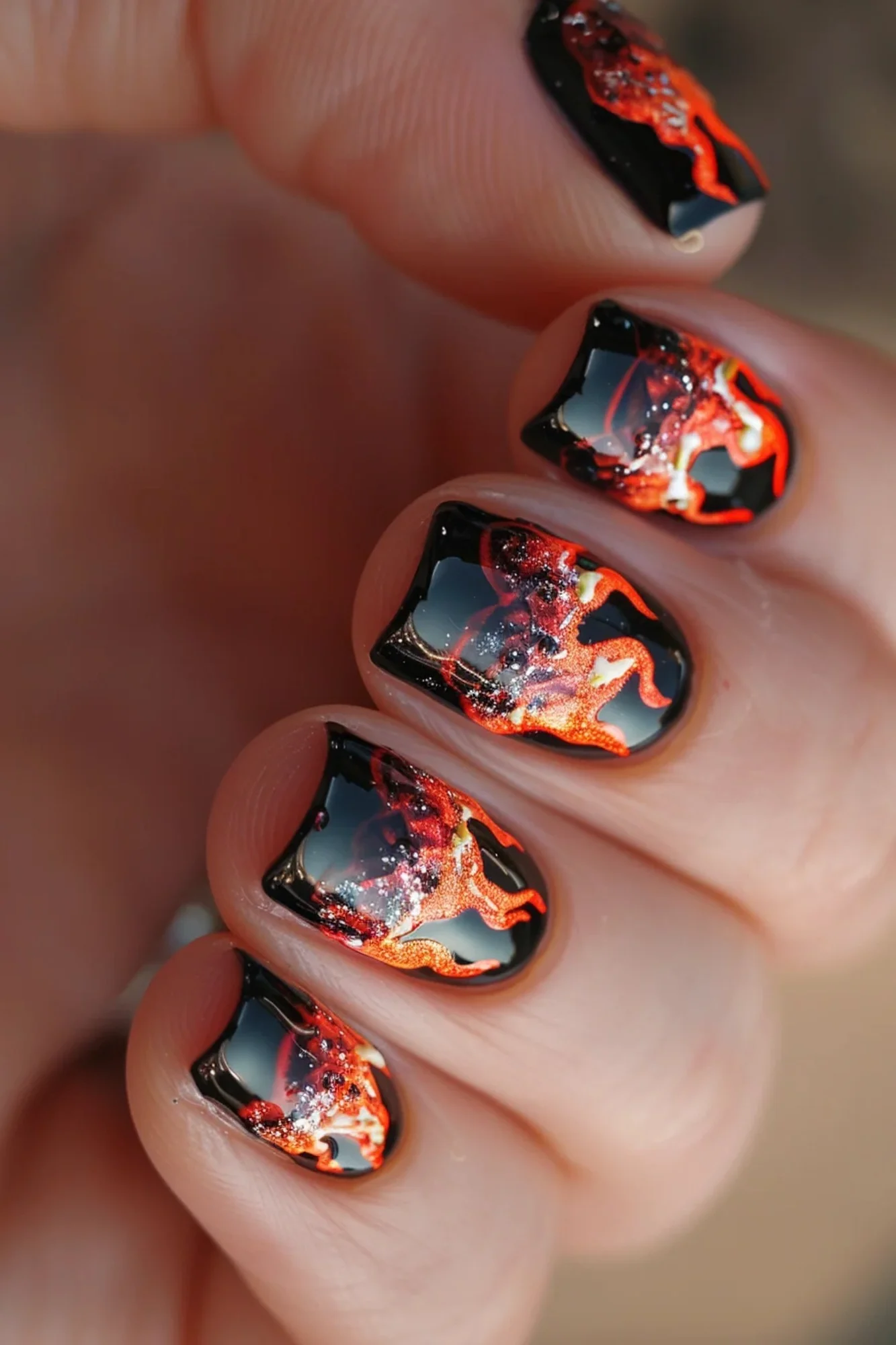 The nails feature a dark base, with flames that are more intricate and detailed. The flames include various shades of orange, yellow, and red, creating a realistic fire effect. 