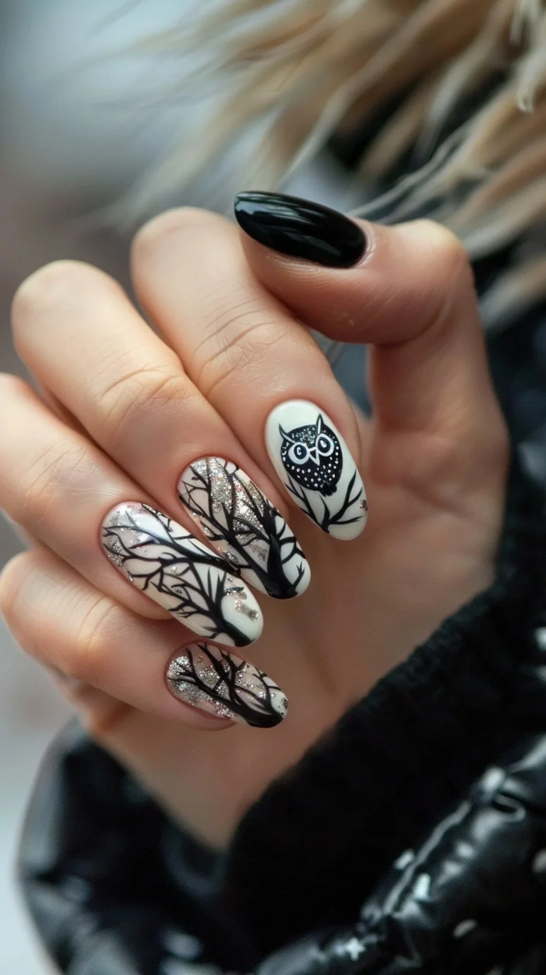 The nails are adorned with a monochrome theme. The base color is white with intricate black tree branch designs extending across the nails. An owl is perched on one of the branches, adding a touch of nature and elegance to the design.