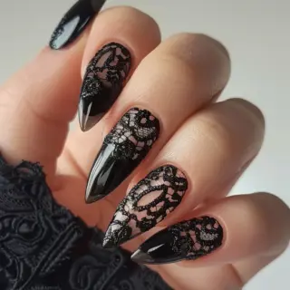 Stiletto-shaped nails combine a glossy black base with intricate black lace designs over a nude background. The lace patterns feature floral motifs, adding an elegant and delicate touch to the bold and sharp shape of the nails, making them stand out.