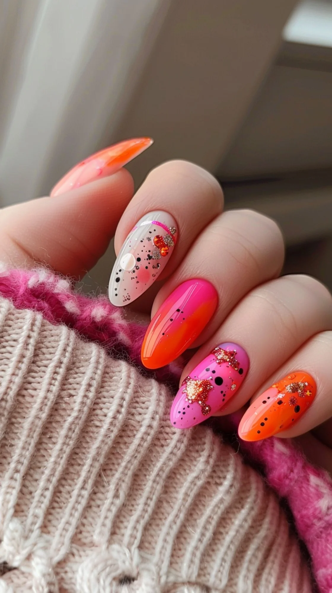 Bright pink and orange nails with bold black accents and glittery details. The strong contrast and sparkles create a striking and stylish summer look.