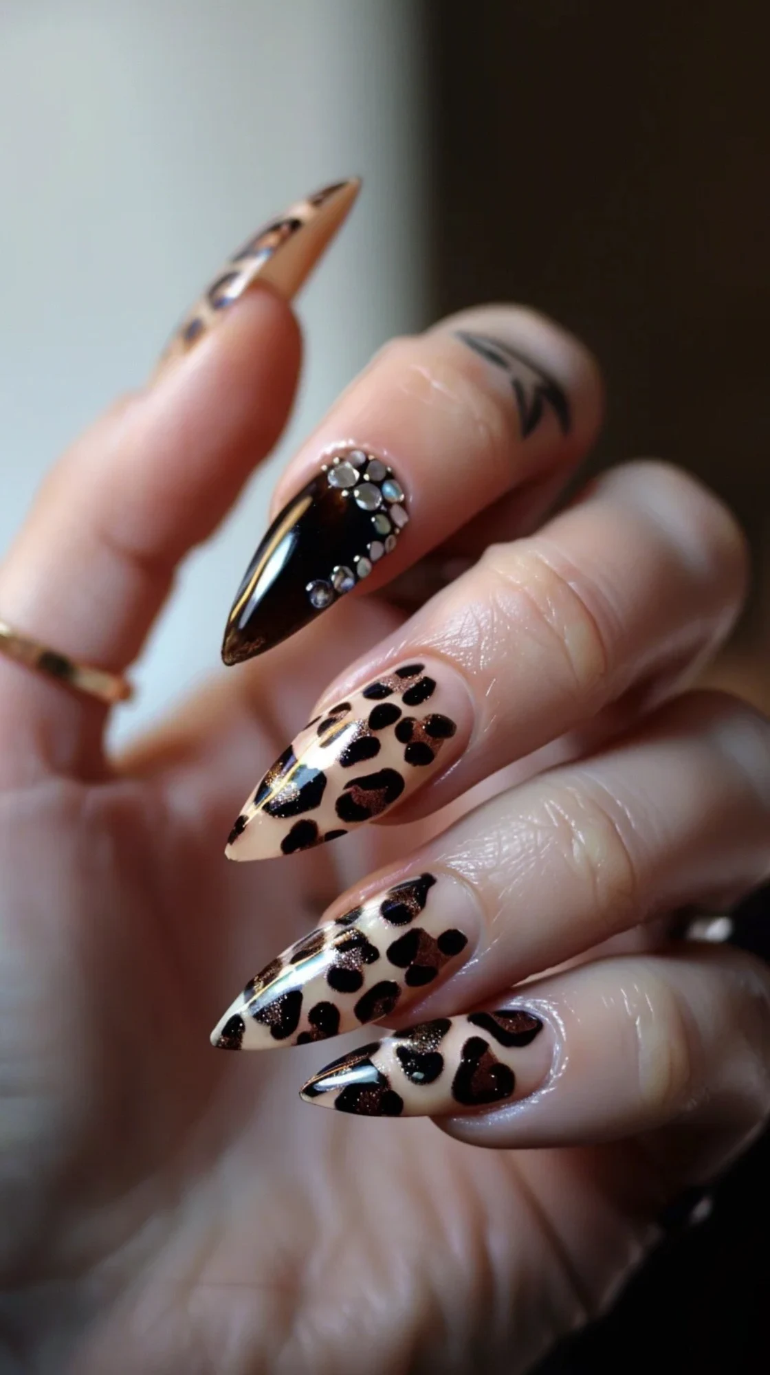 Here are long, stiletto-shaped nails with a nude base color. The leopard print design uses brown and black tones, with one nail featuring intricate rhinestone embellishments. The overall look is sophisticated and edgy, combining elegance with a wild touch.