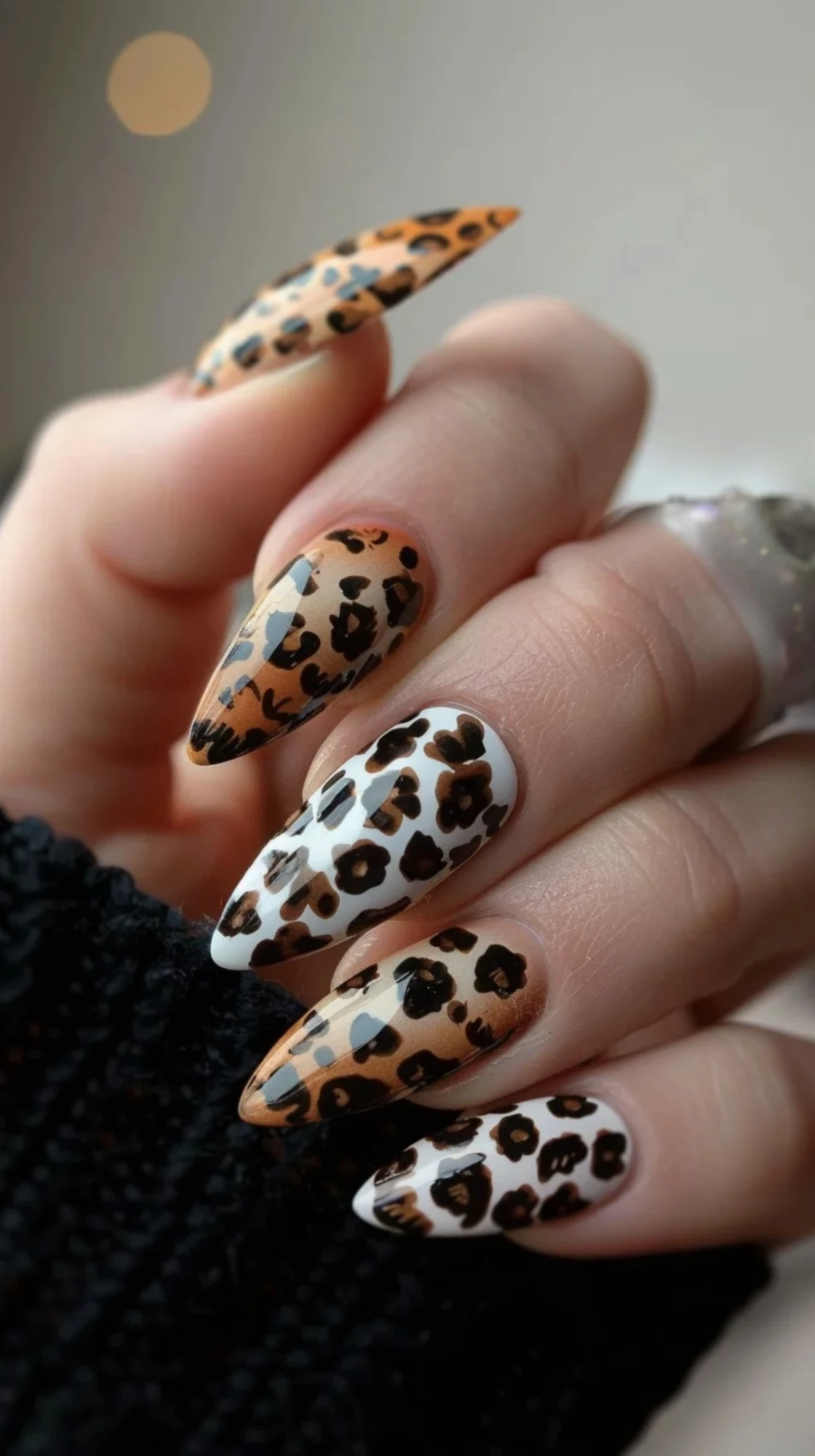 These are long, almond-shaped nails with a mix of white and beige base colors. The leopard print design is done in brown and black, with some nails featuring an ombre effect. The combination of colors and patterns gives a chic and trendy appearance.