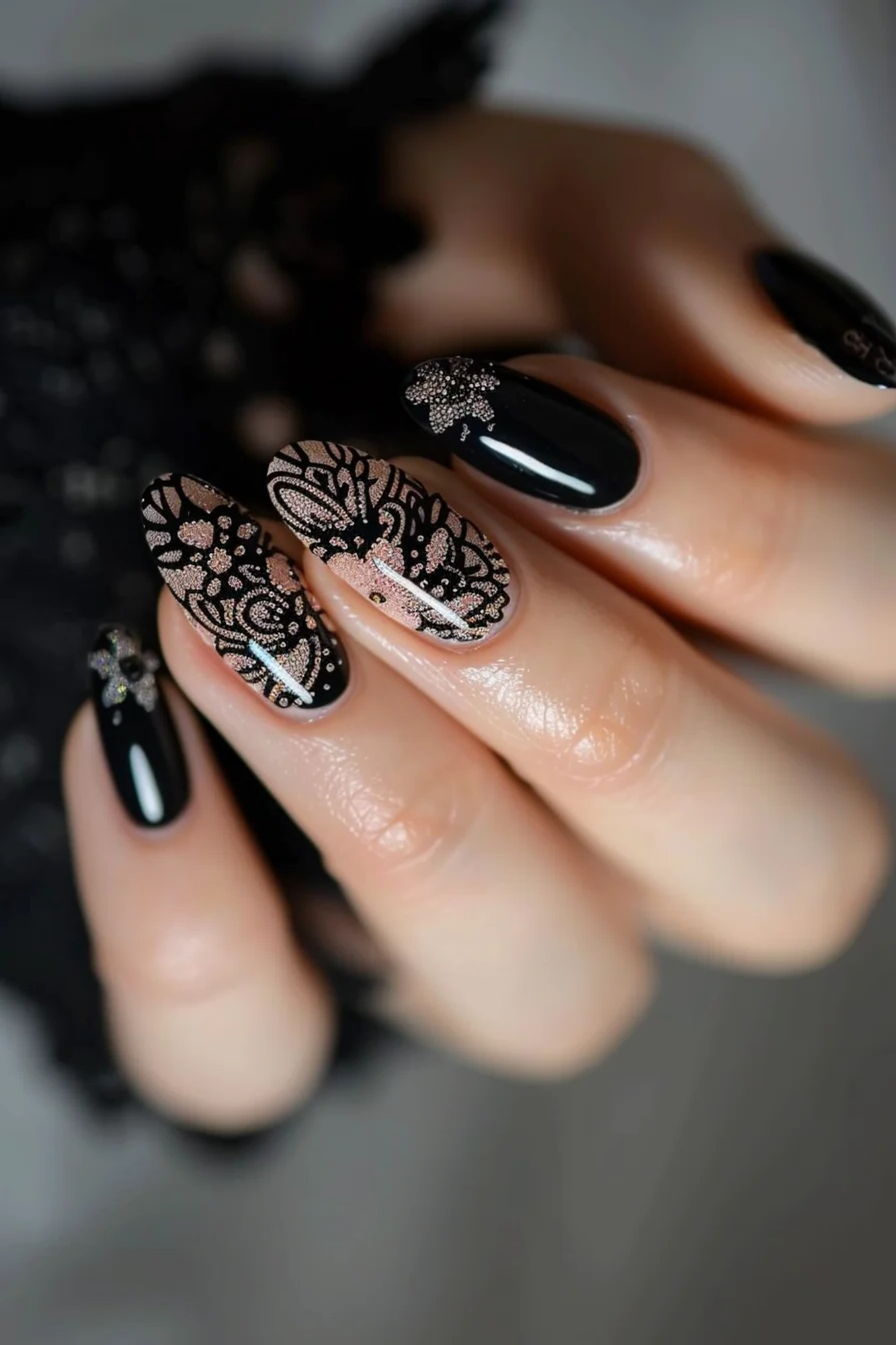 Combining glossy black polish with intricate black lace designs, these almond-shaped nails feature floral and geometric motifs. The lace is detailed with subtle glitter accents, adding a touch of sparkle to the sophisticated and elegant design.
