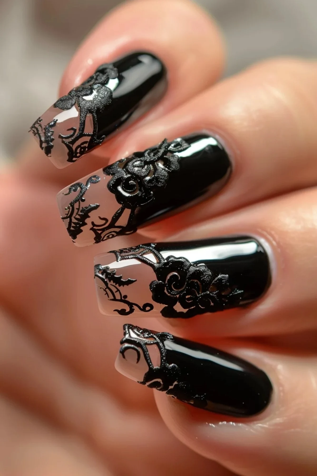 Here are square-shaped nails with a glossy black polish, decorated with intricate black lace designs over a nude base. The lace patterns include floral elements, creating a striking contrast against the black polish, adding depth and texture to the elegant design.