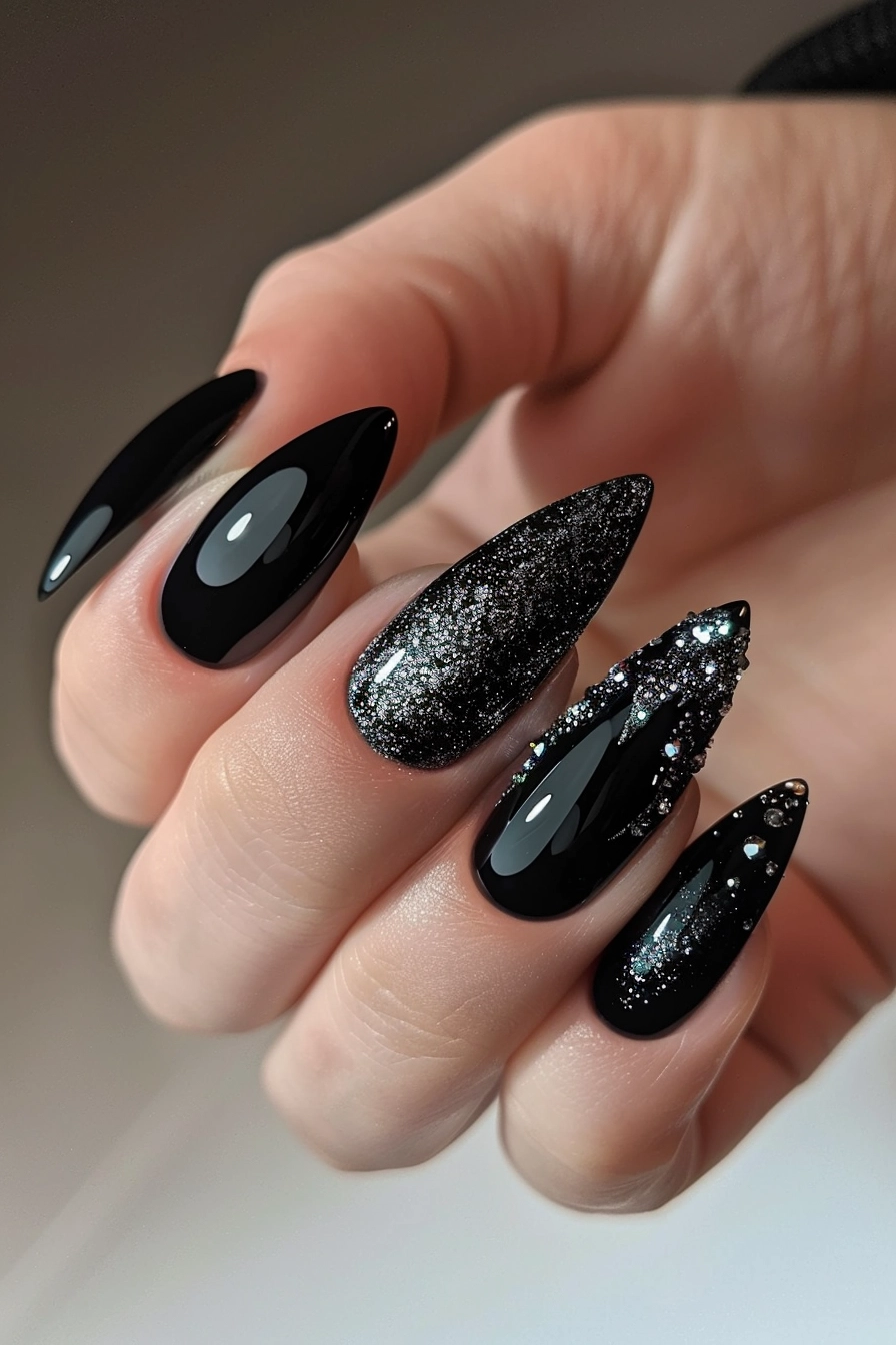 Stiletto-shaped nails in glossy black with an accent of black glitter and rhinestones, creating a dark and dramatic effect.
