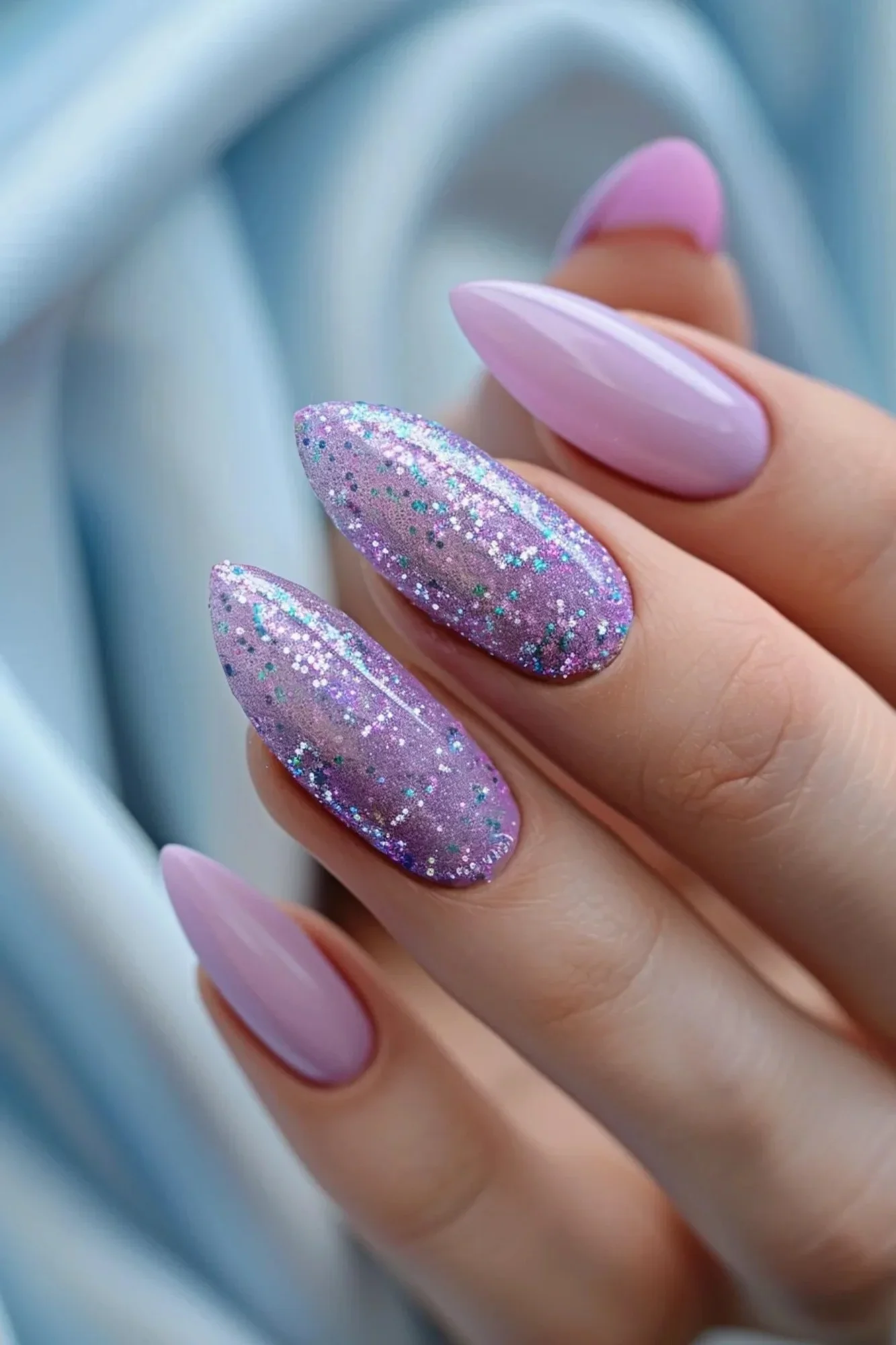 These nails combine a pastel purple base with a gradient of glitter that starts at the cuticles and becomes more intense towards the tips. The glitter includes small, iridescent particles that reflect light beautifully, creating a sparkling effect.