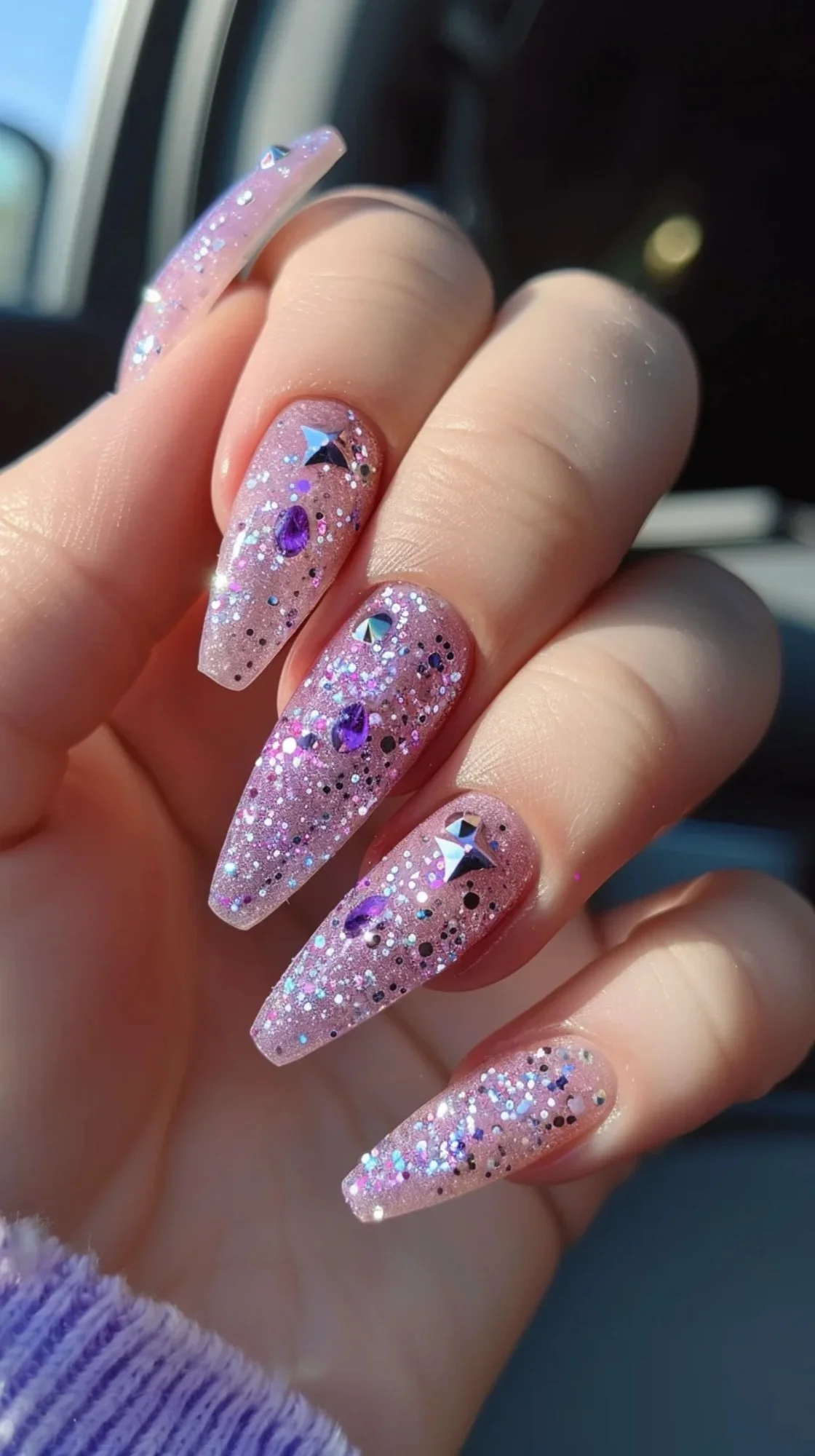 These long nails are adorned with a pinkish-purple base and embellished with glitter and gemstone-like decorations. The addition of tiny stars and heart-shaped glitters adds a whimsical touch, making these nails truly stand out.