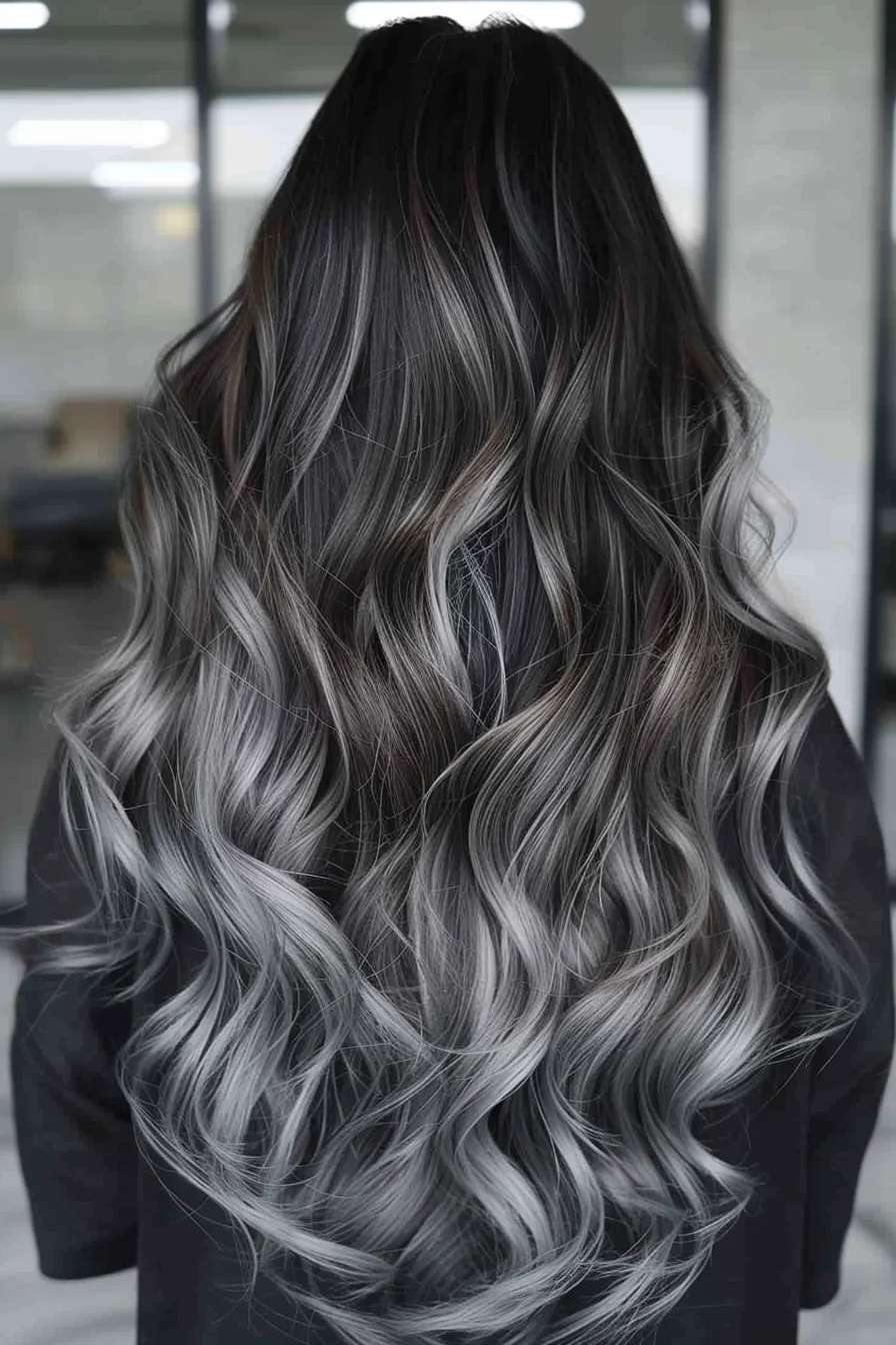 Dramatic and edgy, this long balayage transforms from jet black roots to icy silver ends in a stunning display of contrast. Voluminous waves showcase the seamless color transition, with each curl revealing new depths of smoky gray tones. This avant-garde look is not for the faint of heart, but for those who dare to stand out from the crowd. 